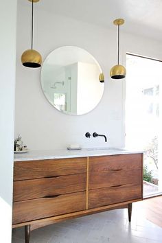 a bathroom vanity with two lights hanging above it and a round mirror on the wall