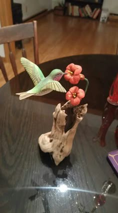 two hummingbirds flying over a piece of driftwood with flowers in it on a table