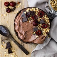 a chocolate dessert with cherries and nuts in it on a wooden table next to spoons