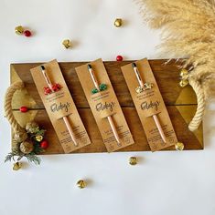 three wooden tags with writing on them sitting next to some christmas decorations and gold bells