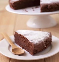 a piece of chocolate cake on a white plate with a wooden spoon next to it