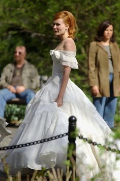 a woman in a white wedding dress walking down the street with other people behind her