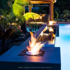 a fire pit in the middle of a pool surrounded by greenery and trees at night