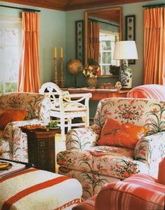 a living room filled with furniture next to a window covered in orange drapes and curtains