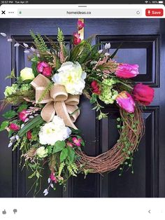 a wreath with flowers and greenery is hanging on the front door's black door