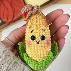 a hand holding a small crocheted toy corn on the cob in it's palm