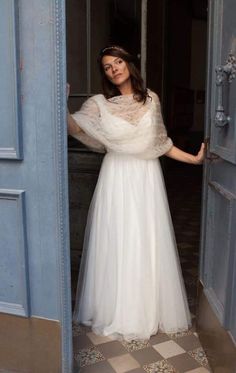 a woman standing in an open doorway wearing a white dress and holding her arms out