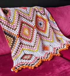 a crocheted granny blanket on a pink couch in front of a black wall