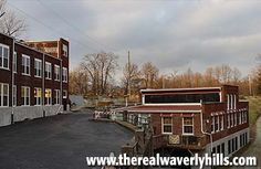 an empty parking lot in front of two brick buildings with windows on each side and one large building behind it