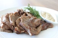 a white plate topped with meat next to a small bowl of ranch dressing on top of it