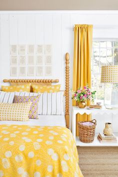 a bedroom with yellow and white bedding, pillows and curtains on the windowsill