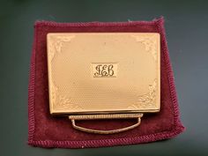 a gold plated pocket watch sitting on top of a red velvet case with monogrammed initials