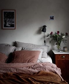 a bed with pink sheets and pillows next to a lamp on a nightstand in a bedroom