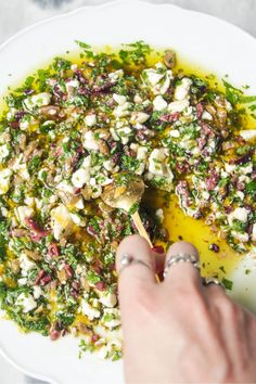 a white plate topped with lots of food next to a person's hand holding a wooden spoon