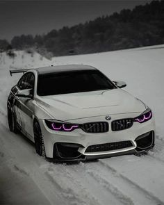 a white car driving down a snow covered road in the middle of winter with its lights on