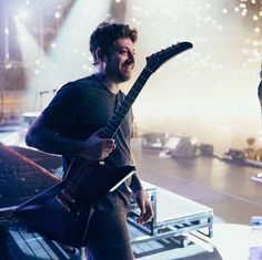 a man holding a guitar while standing on top of a stage with lights behind him