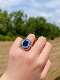 a woman's hand holding a ring with a large blue stone in the center