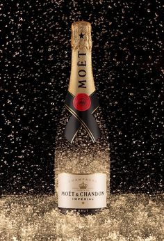 a bottle of champagne is sprinkled with gold dust and water droplets on a black background