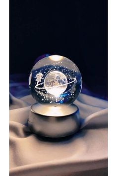 a glass ball with an image of the moon and stars in it sitting on top of a white cloth