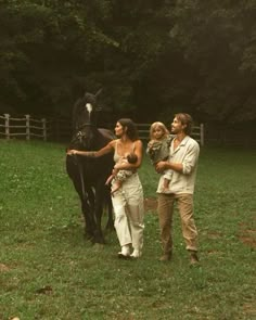 three people are standing in the grass with a horse and another person is holding a baby