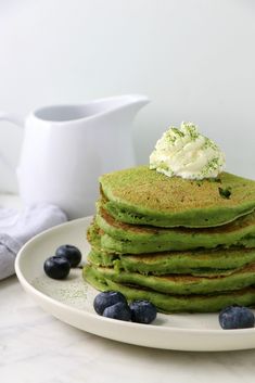 a stack of green pancakes with blueberries and whipped cream