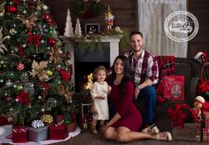 a man and woman sitting next to a small child in front of a christmas tree