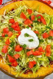 a pizza topped with lettuce, tomatoes and sour cream