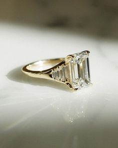 an emerald - cut diamond ring sits on a white surface in this close up photo