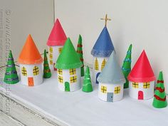 paper houses are lined up on a white surface with christmas trees in the foreground