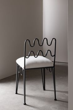 a white chair sitting in front of a wall next to a black metal frame with wavy lines on it