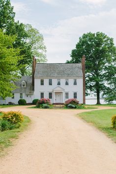 a large white house sitting on top of a lush green field next to a dirt road