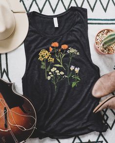 Women's muscle tank cut with low-cut armholes and curved bottom hem. This flowy tank top is featuring a botanical illustration of medicinal plants - Tansy, Calendula, Yarrow, Chamomile, and Wild Pansy. A perfect summer tank with an original watercolor design will make an excellent gift for herbalist, the owner of a medicinal herb garden or anyone interested in medicinal plants. Printed on a Black Heather tank top - Lightweight fabric - 80% rayon, 20% polyester.  How it's made: * All prints are original watercolor designs hand-painted by a botanical artist. * Tanks are printed and shipped by my printing partner in the US, Canada, or Europe. * By buying from this shop, you are directly supporting a woman-owned small business created out of love for plants to educate, inspire and keep us conn Relaxed Fit Tank Top For Spring, Relaxed Fit Spring Tank Top, Spring Graphic Print Cotton Tank Top, Spring Cotton Graphic Print Tank Top, Spring Graphic Tee Sleeveless Top, Summer Graphic Tee Tank Top, Spring Sleeveless Graphic Tee, Sleeveless Spring Graphic Tee, Sleeveless Graphic Tee For Spring