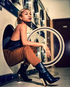 a woman sitting in front of a washer with her legs crossed and looking up