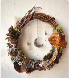 a wreath made out of branches and moss with a crescent hanging from it