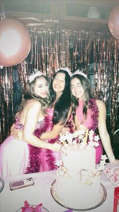 three young women standing next to each other in front of a cake on a table