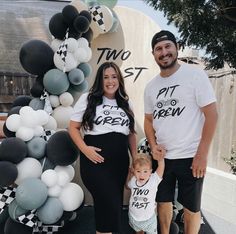 a man and woman standing next to a baby in front of a sign with balloons