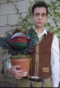 a man holding a potted plant in front of a brick wall