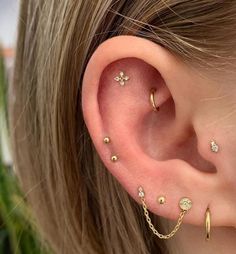 a woman wearing ear piercings with gold chains and diamonds on her ears, in front of