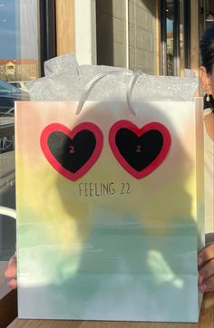 a woman is holding up a shopping bag with two hearts on it that says feeling 22