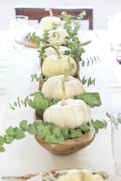 a long table with white pumpkins and greenery