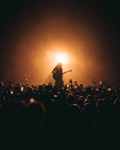 a person standing on top of a stage with a guitar in front of an audience