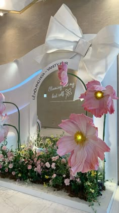 pink flowers and greenery in front of a large white sculpture with a bow at the top