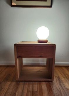 a small wooden table with a light on it's top in front of a wall