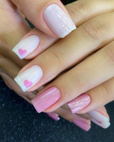 two hands with pink and white manies on their nails, one has hearts painted on it