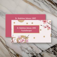 two business cards with pink flowers and gold dots on them sitting on a marble surface