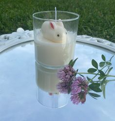 a glass with a candle and some flowers in it on a table outside by the grass