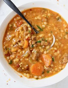 a bowl of soup with carrots, corn and meat in it on a white surface