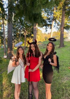 three girls dressed up as devil and angel in the park, one is holding an umbrella