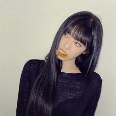 a woman with long black hair wearing a black shirt and eating a donut in front of her face