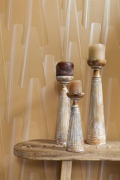 three candles sitting on top of a wooden table in front of a wallpapered background